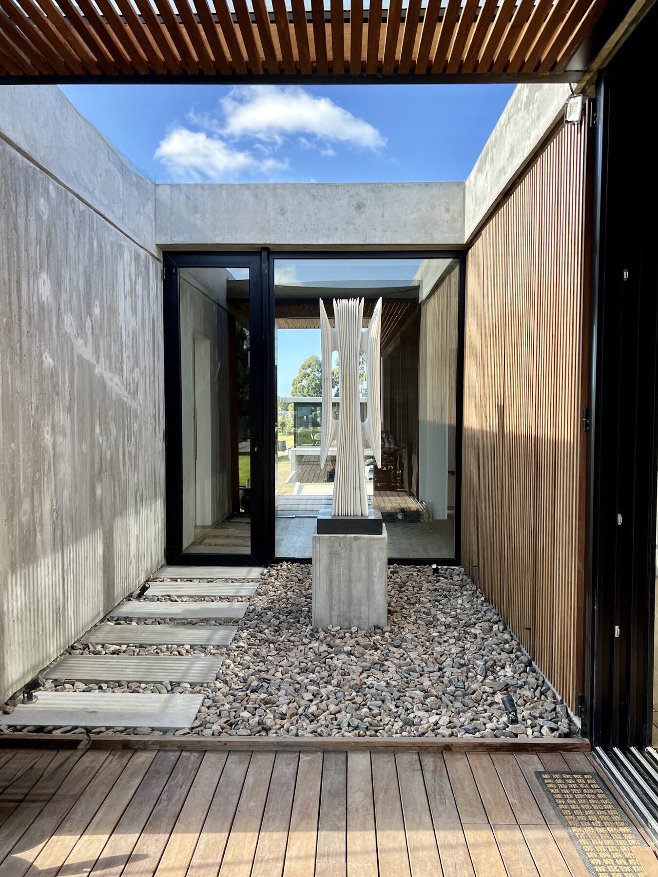 patio de canto rodado y hormigón visto bajo la pérgola de madera