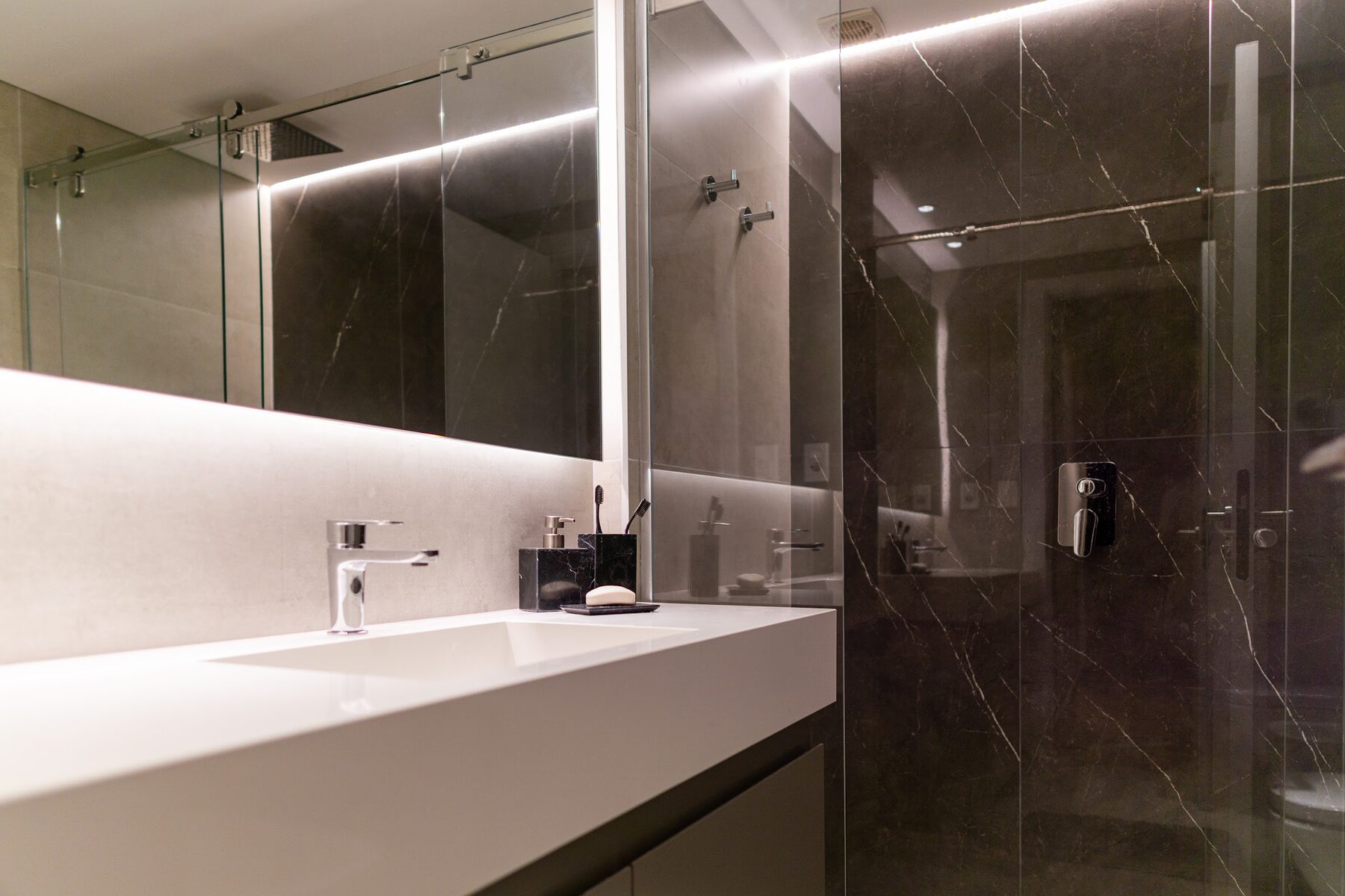 baño con mesada blanca y revestimiento de mármol oscuro