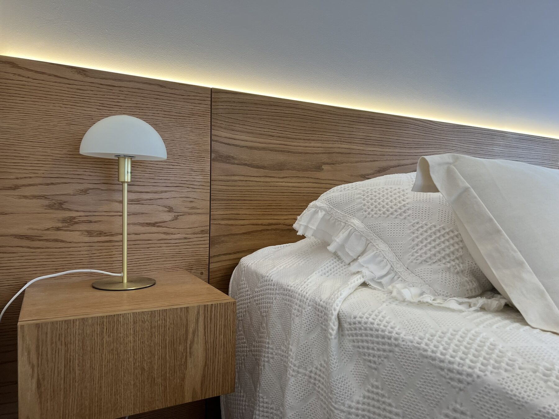 dormitorio con respaldo de roble e iluminación indirecta